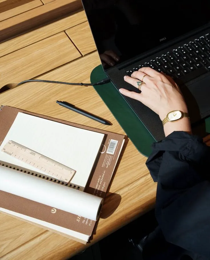 Persona tomando notas en una libreta junto a una laptop sobre un escritorio de madera